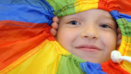 Lapsi kurkistaa värikkään kankaan keskeltä hymyillen