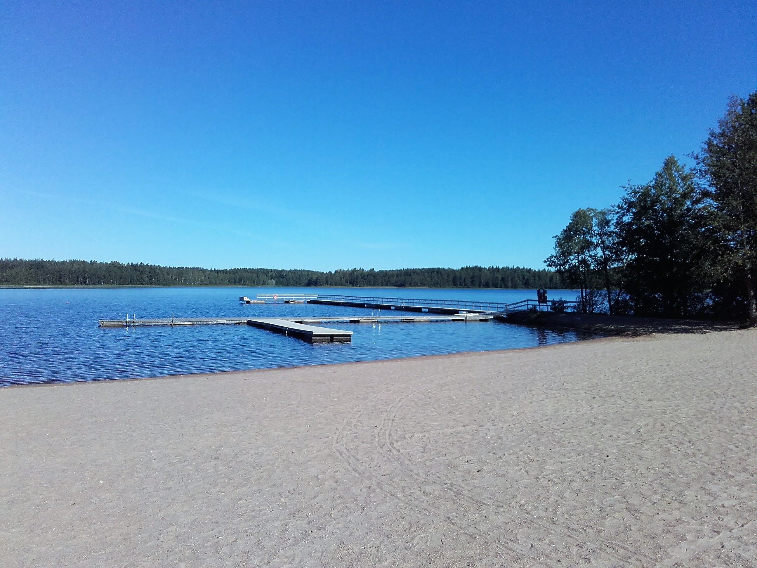 Käyrälammen uimaranta. Kesäinen hiekkaranta. Järvessä pitkä laituri.