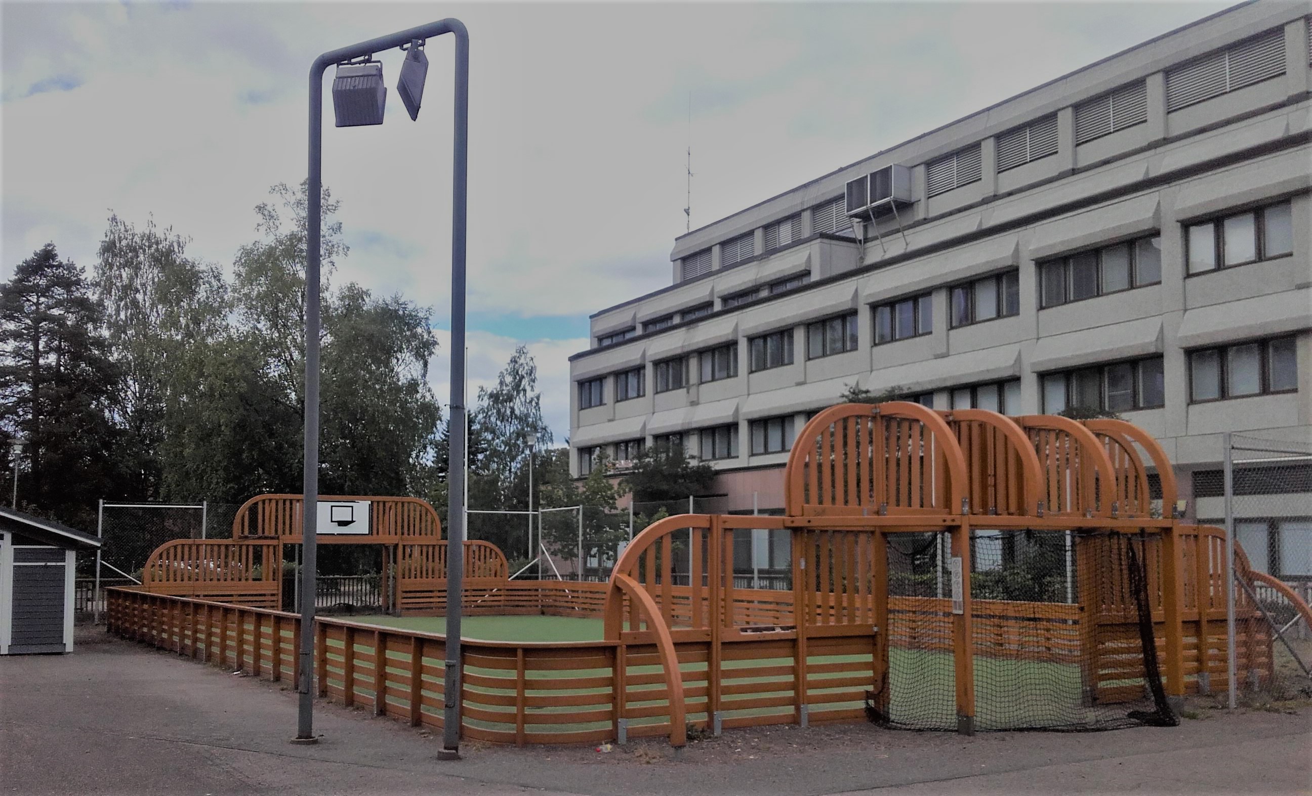 Koulurakennuksen edessä monitoimikenttä. Aidattu tekonurmikenttä. Kentän kummassakin päädyssä koripallotelineet sekä jalkapallomaalit. Kentän laidalla korkea metallinen valaisinpylväs.