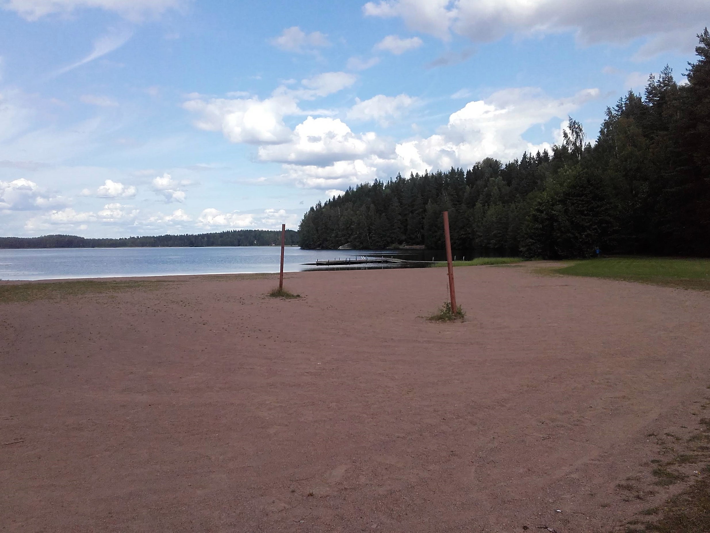 Sompasen uimaranta. Tasainen hiekkaranta. Rannalla tolpat lentopalloverkolle. Taustalla metsää.