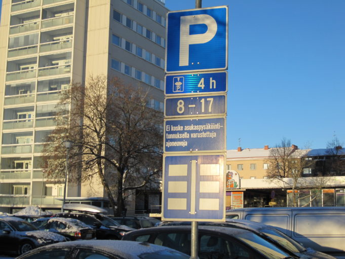 Cars parked in parking lot. Traffic sign explains parking restrictions.