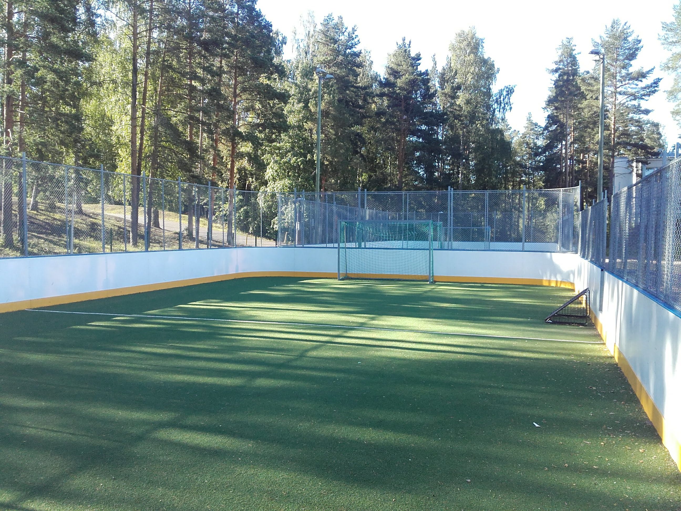 Tekonurmikenttä jossa kaukalon ladiat. Kentän päädyssä jalkapallomaali. Kentän takana kasvaa puita.