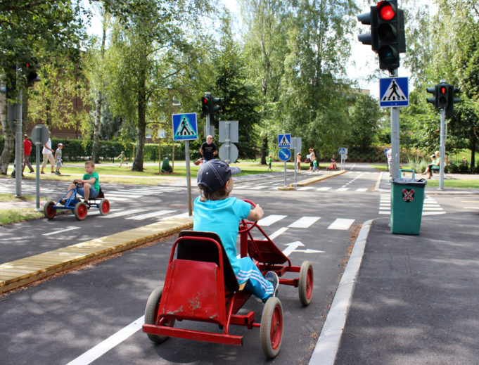 Lapsi ajaa polkuautolla lasten liikennepuistossa pysähtyneenä punaisiin liikennevaloihin.