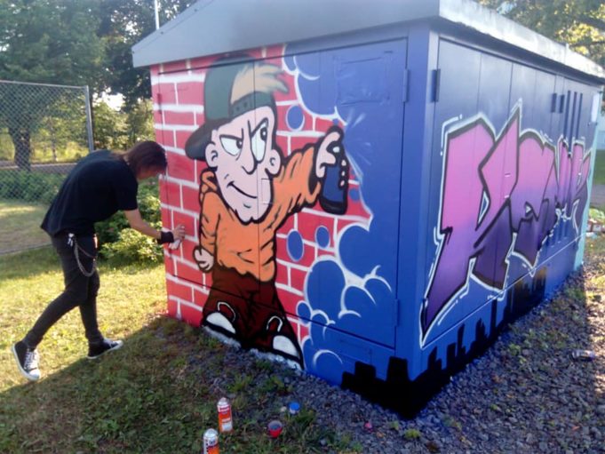 Nuori mies maalaa graffitia muuntamon seinään