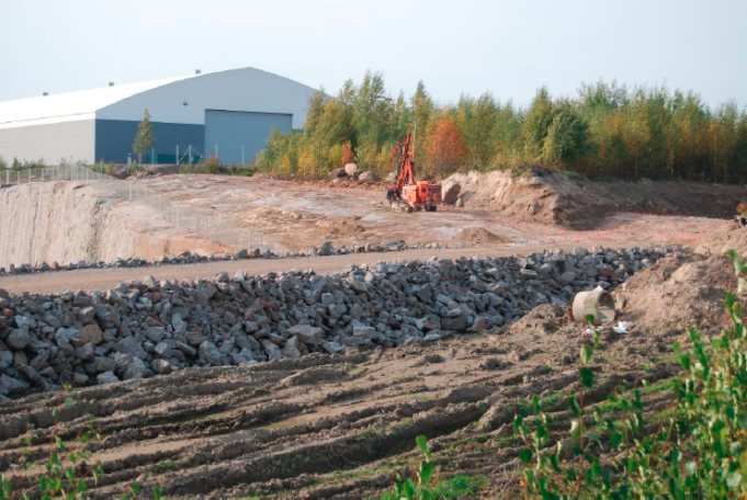 Kouvola Cargo Handling halliRRT-työmaalta nähtynä. Etualalla uuden tien murskepohja. Taustalla oranssi kone, joka poraa kalliota.