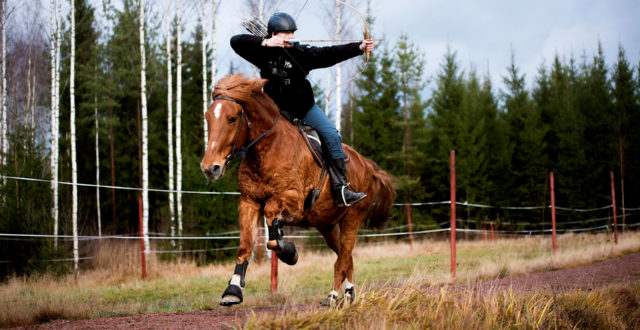 Mies hevosen selässä ja ampuu jousipyssyllä