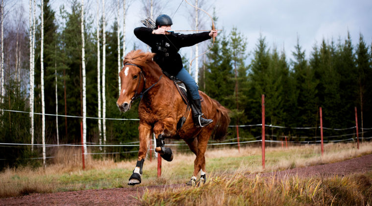 Mies hevosen selässä ja ampuu jousipyssyllä