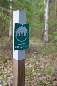 Kuvassa puupaalu, jossa vihreävalkoinen kyltti metsäkuviolla ja tekstillä "luonnonsuojelualue".