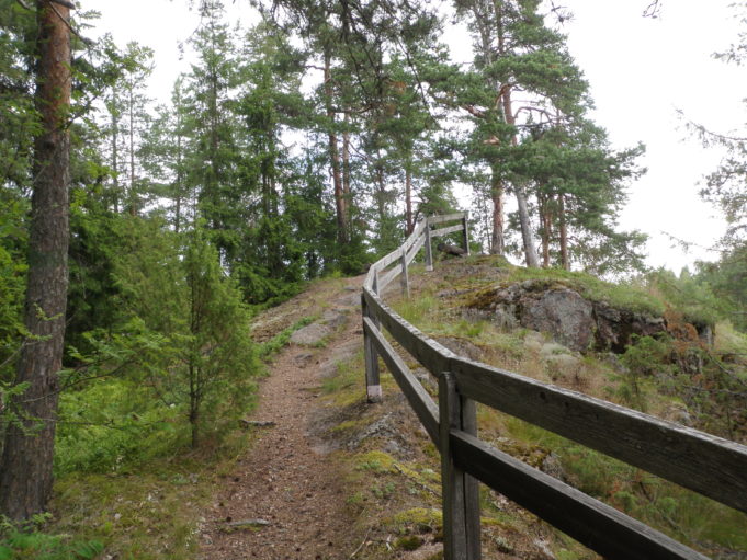 Kuvassa polku kulkee kallion päälle. Polun oikealla puolella kulkee puinen turva-aita.