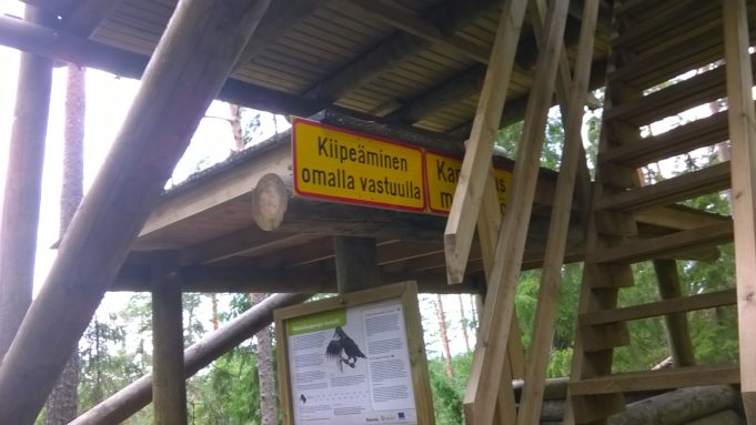 Kuvassa puisia luontotornin rakenteita ja kyltti tekstillä "Kiipeäminen omalla vastuulla".