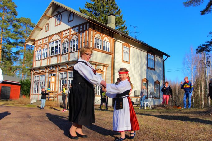 Nainen ja tyttö tanssivat käsi kädessä. Tytöllä kansallispuku.