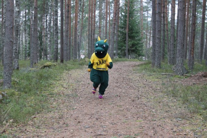 Liikuntamaskotti Kääkki juoksee metsässä polkua pitkin.