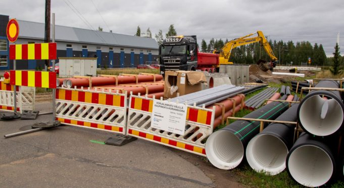 Katu- ja vesirakennustyömaa. Kuorma-auto, kaivinkone, vesiputkia, pilvinen sää.