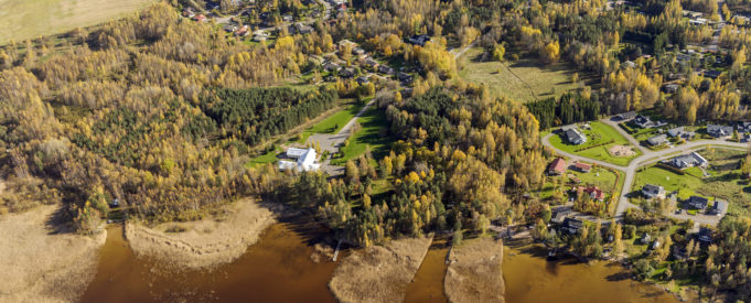 Ilmakuva, jossa näkyvissä järven rantaa, metsiköitä ja muutamia asuinalueita.