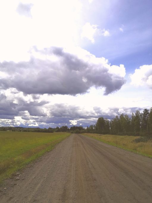 Leveä hiekkatie pellon ja puiden keskellä kesäpäivänä Valkealassa.