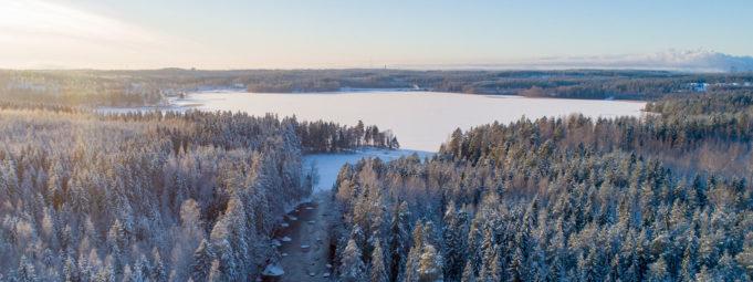 Ilmakuva Käyrälammesta ja lähitienoosta talvella. Puita, joki ja luminen järvi.