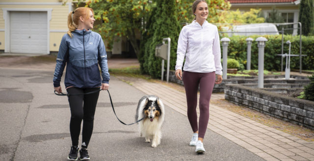 Kaksi naista ulkoiluttaa koiraa asuinalueella.