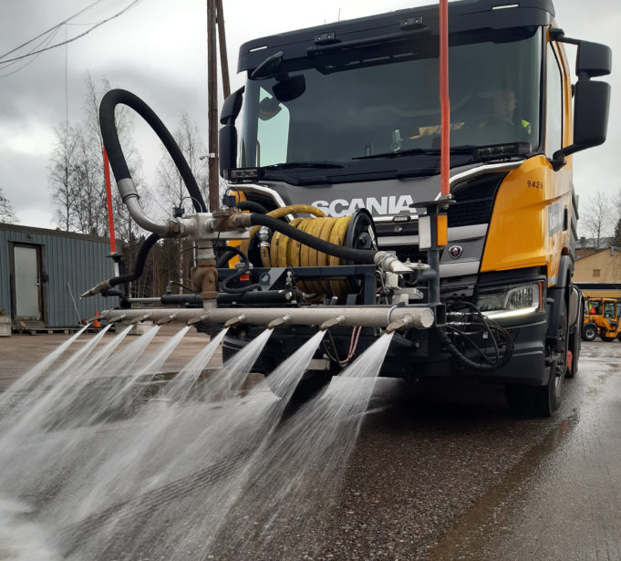 Kuorma-auto suihkuttaa vettä kadulle hiekan poistoa varten