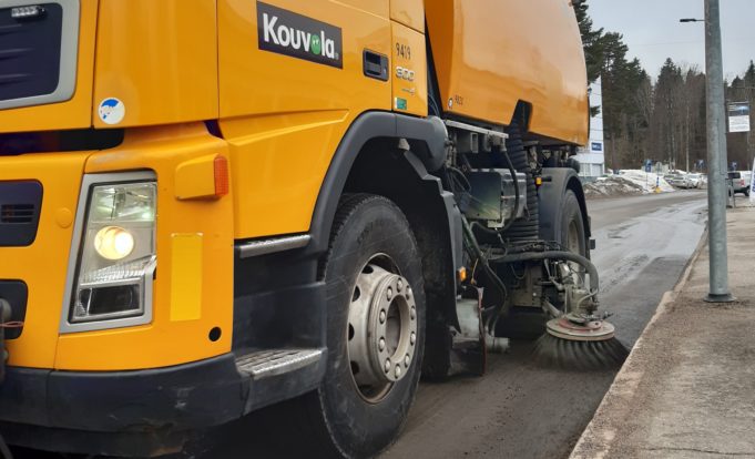 Keltainen kuorma-auto harjaa kadulta hiekkaa.