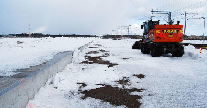 Työkone poistaa lunta RRT-ratapohjalta betonilaiturin vierestä.