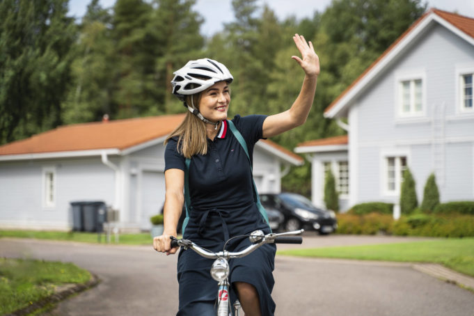 Nainen ajaa pyörää omakotitaloalueella ja tervehtii 