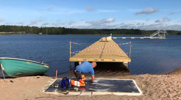 Mies tekee asennustöitä ison laiturin edustalla.