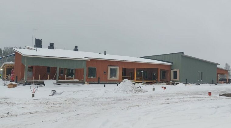 rakenteilla oleva iso puurakennus, harmaa taivas, lunta maassa