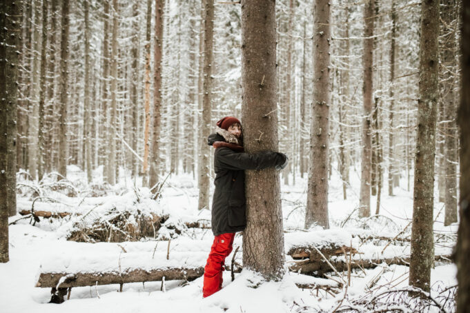 Nainen halaa puuta talvisessa metsässä.