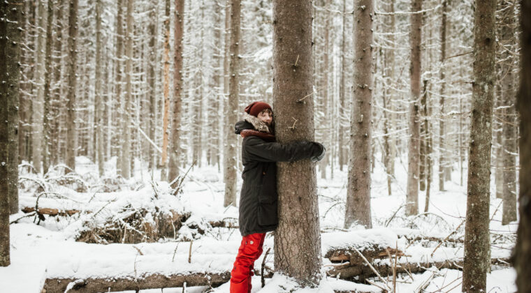 Nainen halaa puuta talvisessa metsässä.