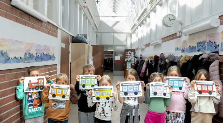 Viisi lasta seisoo koulun käytävällä kasvojen edessä kuva junan eri vaunuista. Veturi ja vaunut kuvastavat joustavan esi- ja alkuopetuksen (JEA) eri osia.