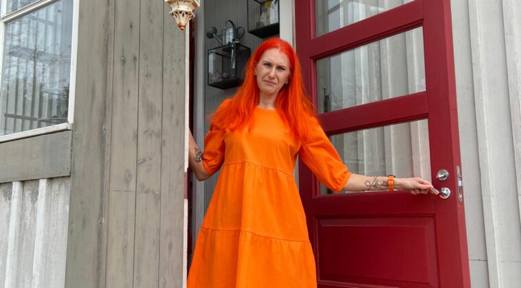Johanna Anttonen oranssissa mekossaan punaisella ovella.
