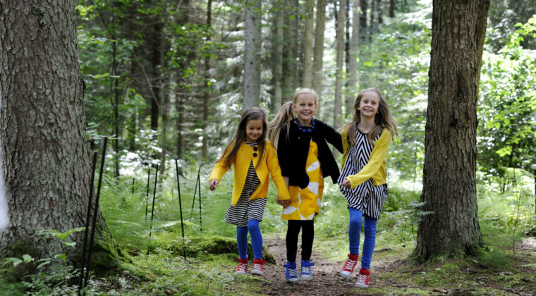 Kolme tyttöä juoksee metsässä.