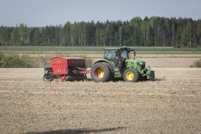 Kevätkylvö pellolla, traktori liikkeellä kylvökoneen kanssa.