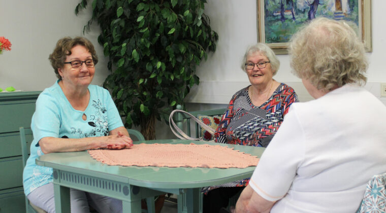 Kolme naista istuu pöydän ääressä juttelemassa