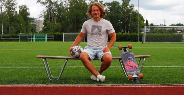 Mies istuu urheilukentän laidalla penkillä jalkapallo vieressään.