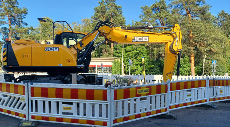 Keltainen kaivinkone tietyömaalla. Ympärillä työmaa-aitoja.