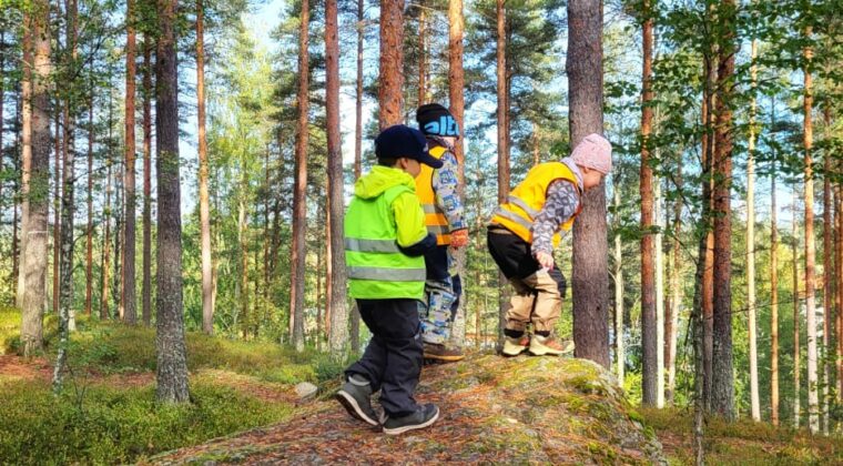 Lapsia kiipeilemässä isolla kivellä syksyisessä metsässä