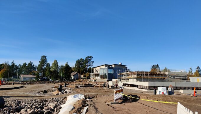 Rakennustyömaa jossa tehdään rakennuksen perustuksia. Sininen taivas. Taustalla rakennus.