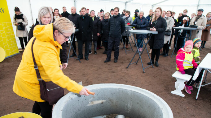 Keltatakkinen henkilö laittaa betonilaastia ison betonirenkaan sisään. Taustalla yleisöä.