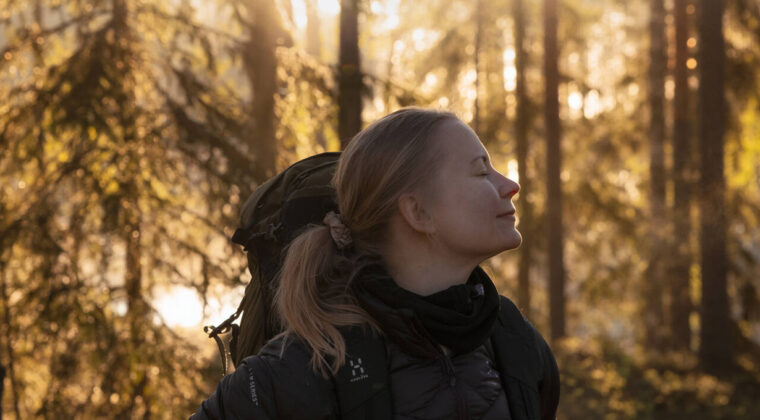 Nainen hymyilee silmät suljettuina syksyisessä metsässä.