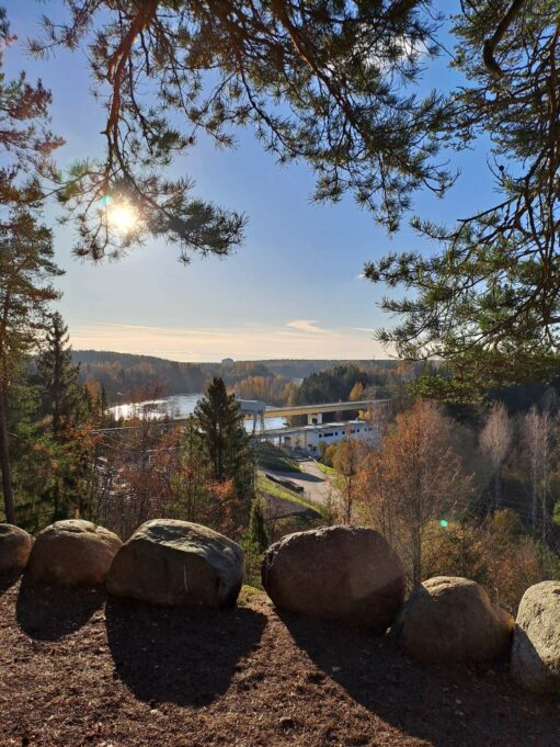 Suuret kivet reunustaa maisemapaikkaa korkealla mäellä. Alhaalla Kymijoen rannassa näkyy voimalaitosrakennus.