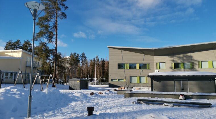 Iso harmaa koulurakennus, kirkas, sininen taivas, luminen maisema.