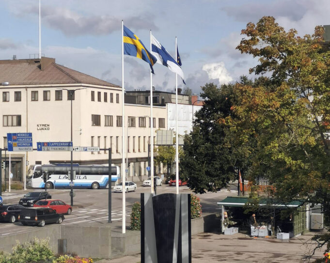 Kouvolan kaupungintalon edustalle olevat kolme lipputankoa. Ensimmäisessä liehuu Ruotsin lippu, seuraavassa Suomen ja viimeisessä EU:n. Taustalla näkyy vaalean ruskea rakennus, liikennettä ja puita.