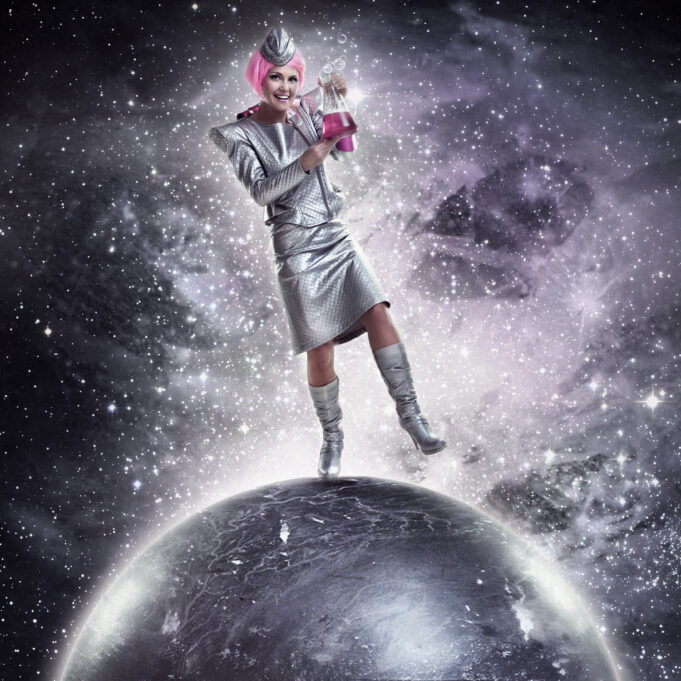Tutkijan näköinen nainen pinkissä tukassa seisoo hopeisen maapallon päällä avaruudessa.