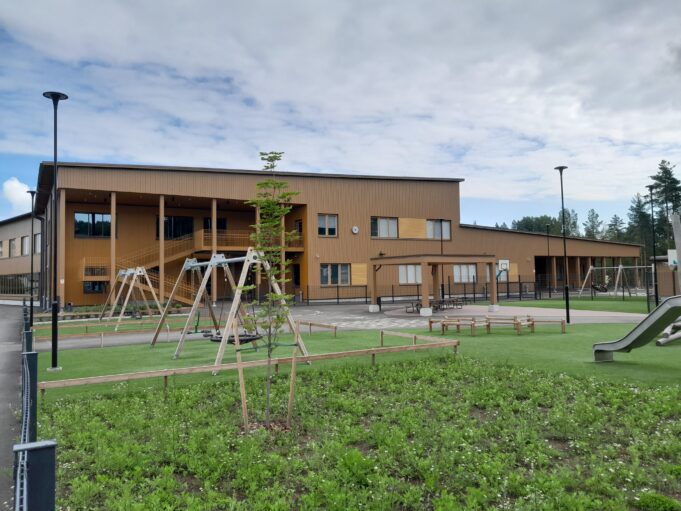 Keltaruskea suurikokoinen Valkealan monitoimitalo. Edessä nurmikkoa ja lasten leikkivälineitä.