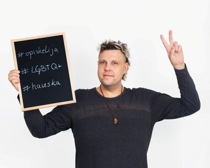 Henkilö pitää oikeassa kädessään kylttiä, jossa lukee #opiskelija #LGBTQ+ #hauska