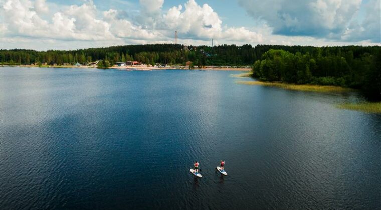 Kaksi henkilöä sup-lautailee suurella lammella