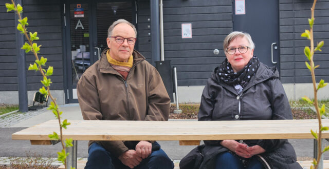 Anne Simpanen ja Jukka Vainio istuvat kotinsa ulko-oven edustalla piha tuolilla. Etualalla pöytä ja kasveja.