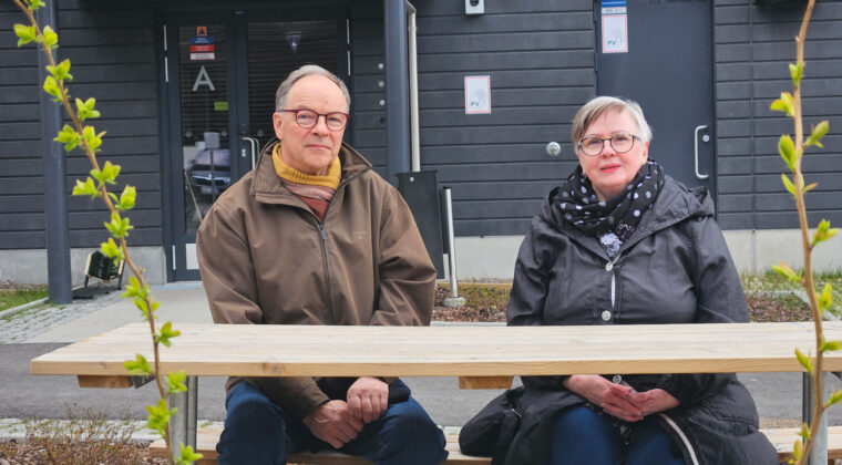 Anne Simpanen ja Jukka Vainio istuvat kotinsa ulko-oven edustalla piha tuolilla. Etualalla pöytä ja kasveja.