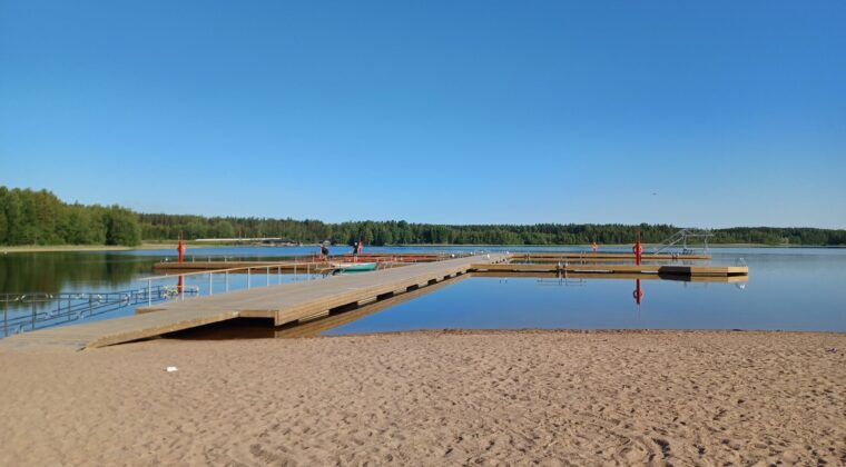 Hiekkaranta ja pitkä puinen laituiri. Kirkas sininen taivas.